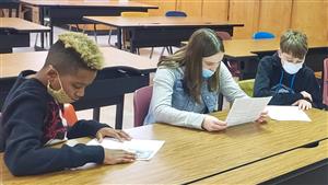 Photo shows three SV students at a table hunched over latest edition of Colonel Chronicles.